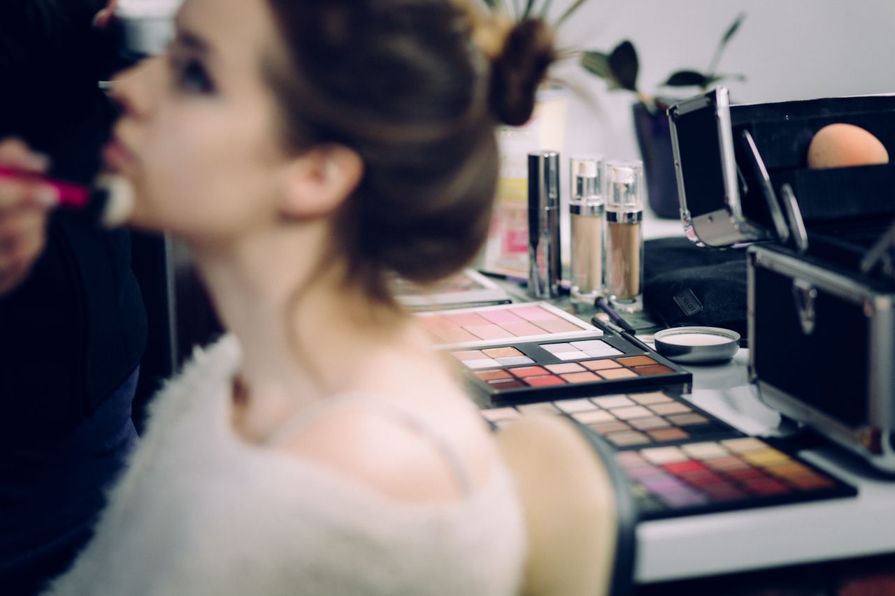 Home A woman receiving professional makeup in a studio with various cosmetics in focus.