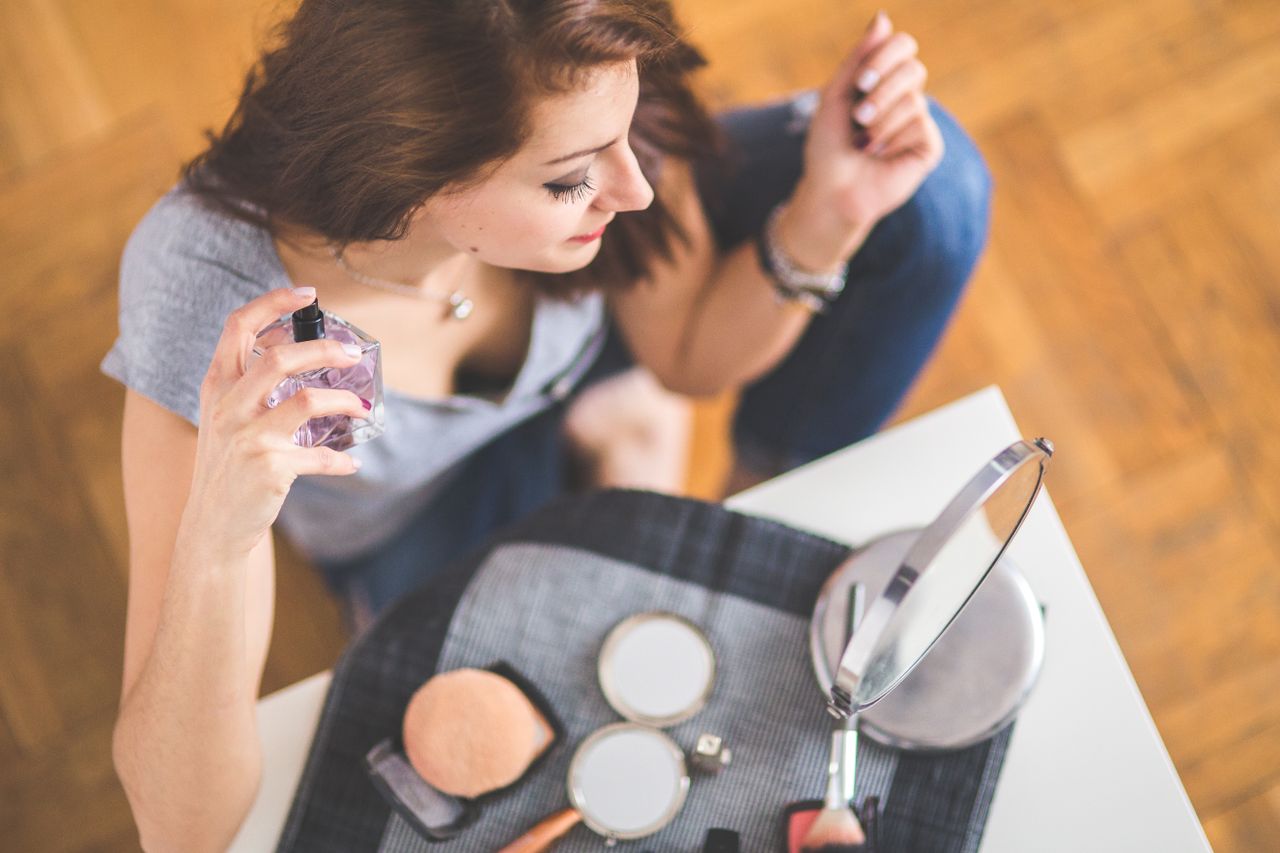 Young woman applying perfume with makeup essentials around her.